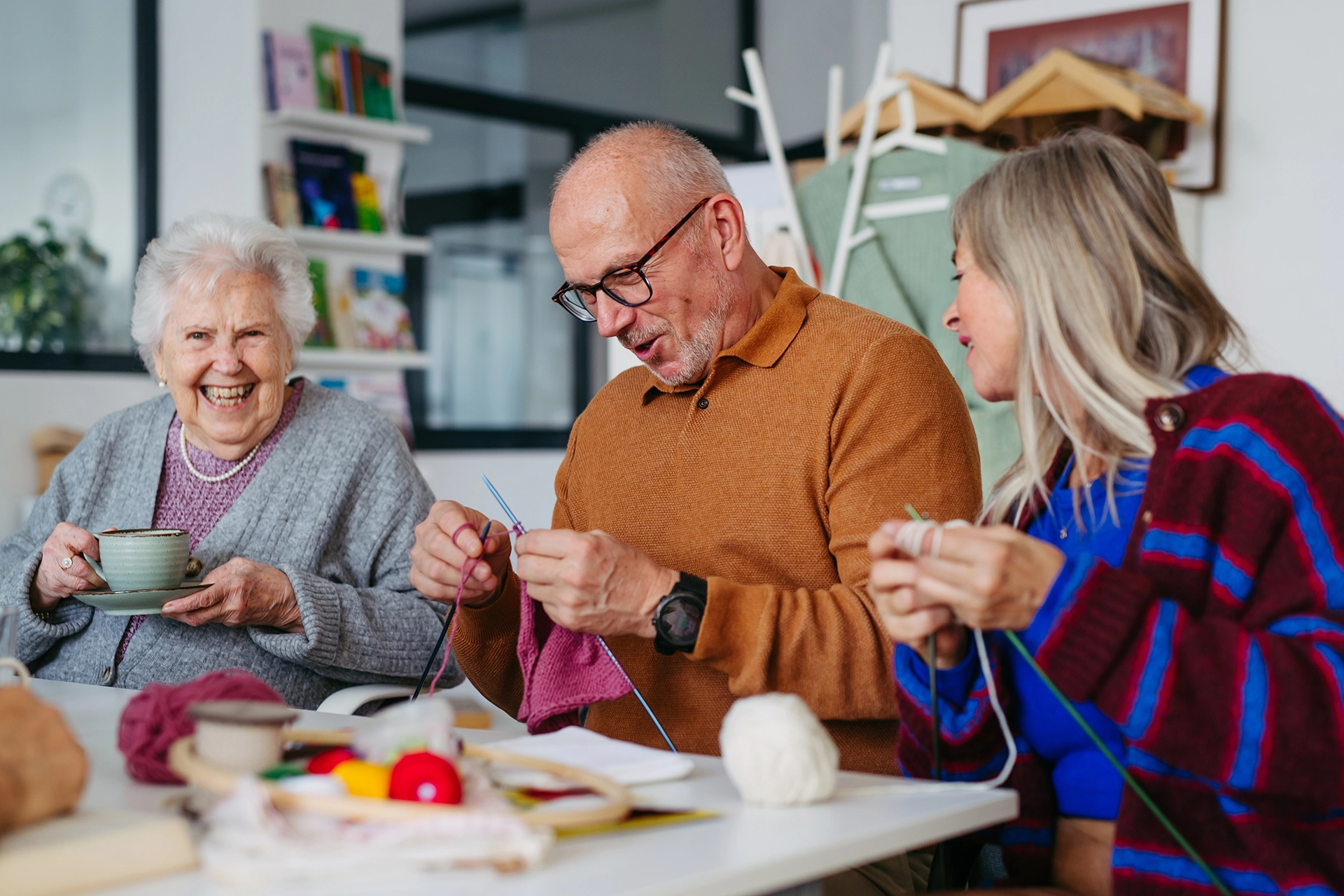 A group of seniors laughing and knitting together around a table